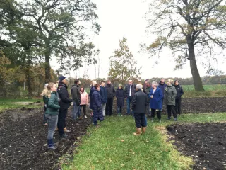 Een groep mensen buiten op het gras, luisterend naar degene die de rondleiding geeft